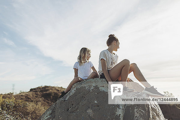 Zwei Mädchen sitzen auf einem Felsen und schauen hinaus; Los Angeles  Kalifornien  Vereinigte Staaten von Amerika