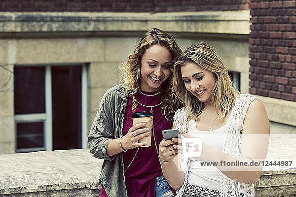 Zwei Studentinnen stehen zusammen auf dem Campus und schauen auf ein Smartphone  Edmonton  Alberta  Kanada