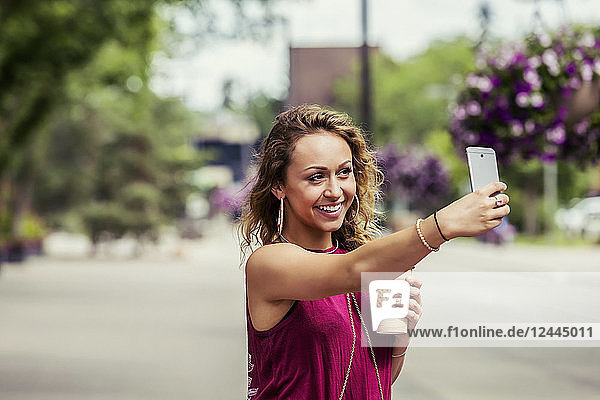A young beautiful woman takes a self-portrait on a cell phone on a street near a university campus  Edmonton  Alberta  Canada