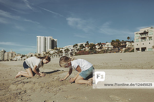 Zwei Mädchen spielen im Sand am Strand mit Wohngebäuden im Hintergrund; Long Beach  Kalifornien  Vereinigte Staaten von Amerika