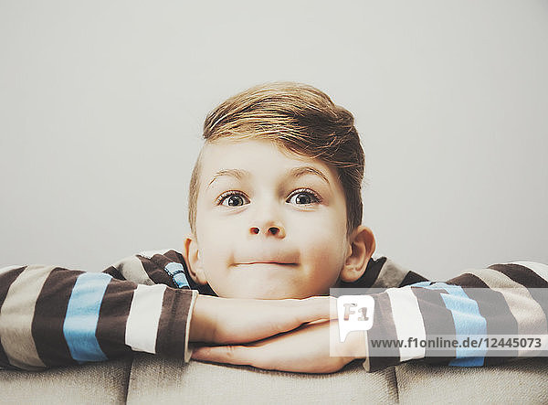Porträt eines kleinen Jungen  der mit zufriedenem Blick und verschränkten Armen hinter einer Couch hervorschaut; Langley  British Columbia  Kanada
