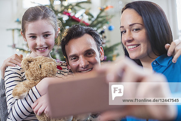 Glückliche Familie mit Smartphone  die ein Selfie im Weihnachtswohnzimmer macht
