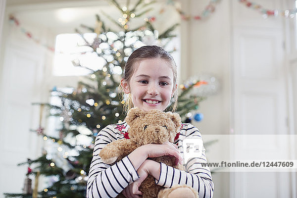 Porträt lächelnd  süßes Mädchen hält Teddybär vor Weihnachtsbaum
