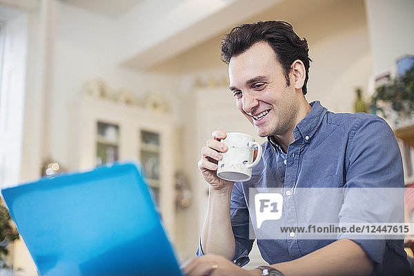 Lächelnder Mann trinkt Kaffee und arbeitet am Laptop