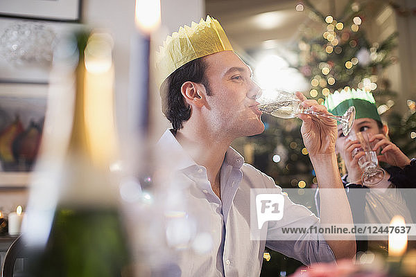 Tochter beobachtet glücklichen Vater mit Papierkrone  der beim Weihnachtsessen Champagner trinkt