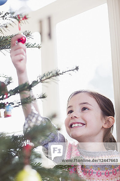 Lächelndes  neugieriges Mädchen  das ein Ornament am Weihnachtsbaum berührt
