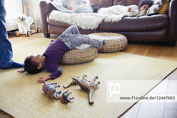 Verspielter Junge mit Dinosaurier-Spielzeug auf dem Boden im Wohnzimmer