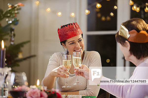 Daughter and senior mother in paper crowns toasting champagne glasses at Christmas dinner table