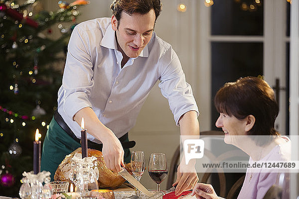 Son serving Christmas turkey to senior mother at candlelight dinner table