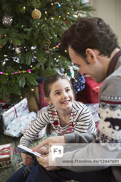 Vater liest mit Tochter am Weihnachtsbaum ein Buch