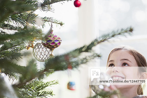 Lächelndes Mädchen mit Blick auf den Schmuck am Weihnachtsbaum