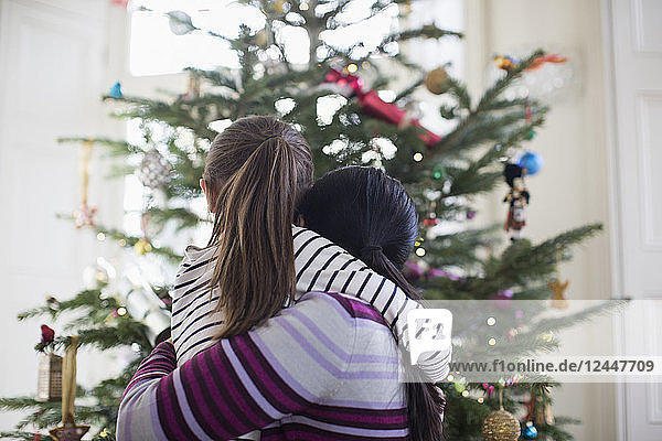 Zärtliche Mutter und Tochter umarmen sich vor dem Weihnachtsbaum