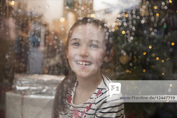Porträt glückliches Mädchen an nassem Fenster im Weihnachtswohnzimmer
