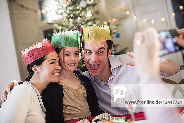 Verspielte Familie mit Papierkronen posiert für ein Foto am Weihnachtstisch