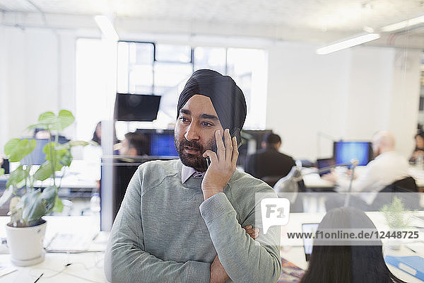 Serious Indian businessman in turban talking on smart phone in office