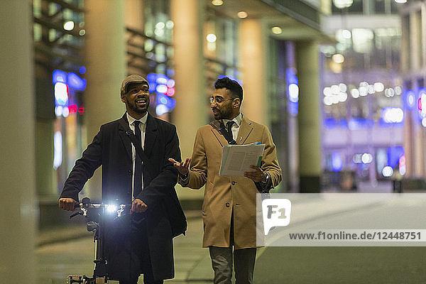 Businessmen talking  discussing paperwork on urban sidewalk at night