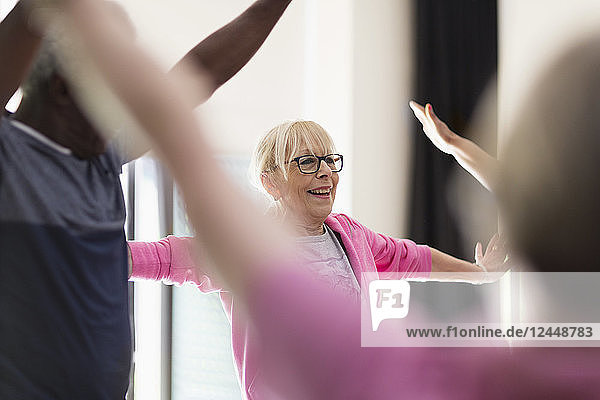 Smiling active senior woman stretching arms in exercise class