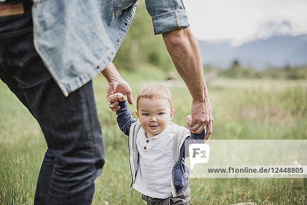 Father walking with baby son in grassy field