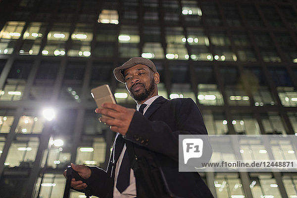 Businessman with smart phone standing below urban highrise at night