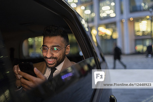 Businessman using smart phone in crowdsourced taxi at night