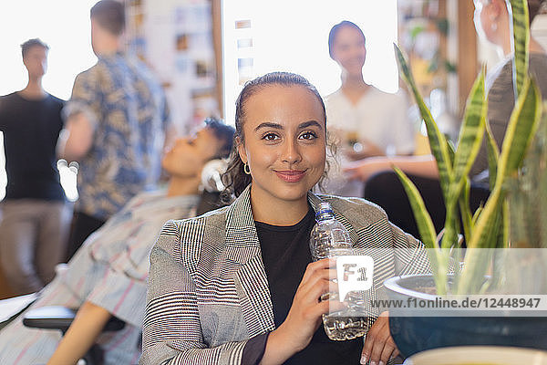 Portrait confident businesswoman drinking bottled water in office