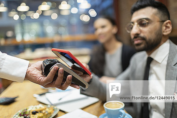 Businessman in cafe paying with smart phone contactless payment