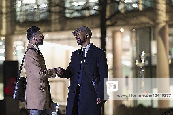 Businessmen handshaking on urban street at night