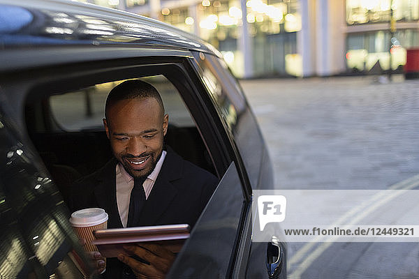 Businessman drinking coffee and using digital tablet in crowdsourced taxi