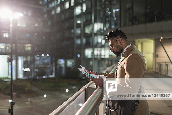 Businessman reviewing paperwork on urban pedestrian bridge at night