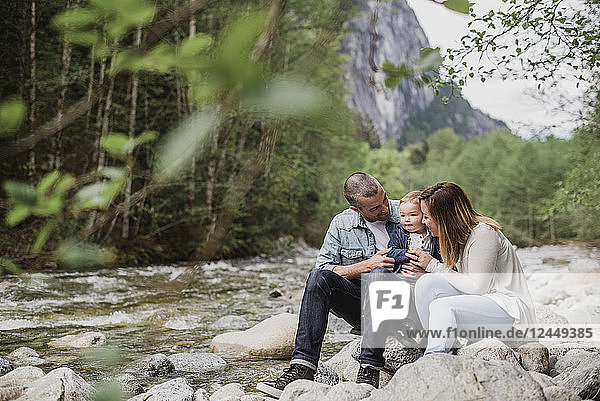 Parents and baby son sitting on rocks along stream