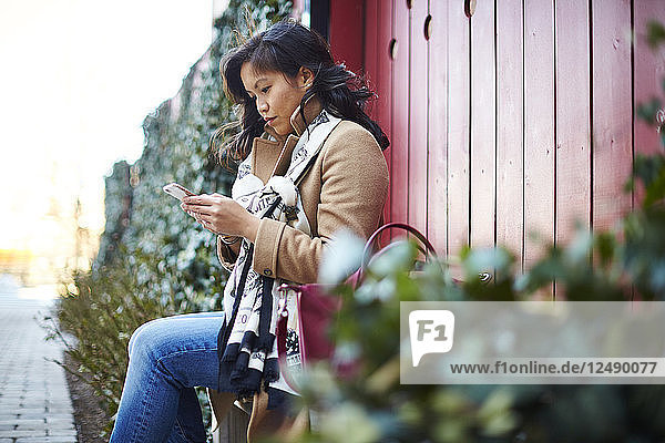 Eine junge asiatische Frau an ihrem Smartphone.
