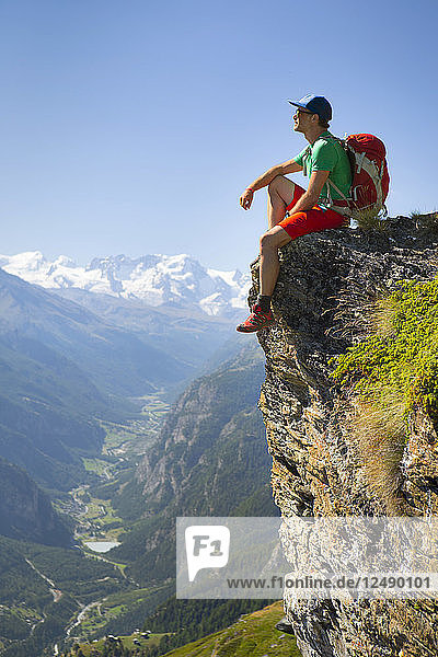 A Hiker Is Taking A Rest At A Steep Rock Face Above The Matterhorn Valley