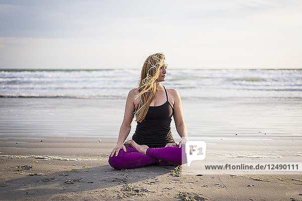 Frau sitzt am Strand und macht Yoga in Rhode Island an einem windigen Tag
