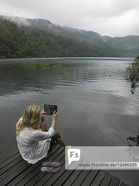 Woman takes photo with tablet on dock in mountain lake