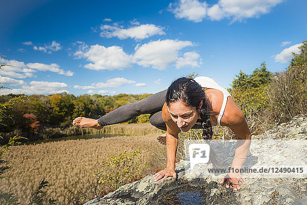 Frau beim Yoga auf einem Felsen sitzend  umgeben von einem Feld