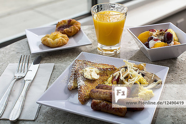 Ein Frühstückstisch ist schön dekoriert mit Toastbrot  Wurst  Käse  Fruchtpudding  gebackenem Kuchen und einem Glas Mango-Shake.