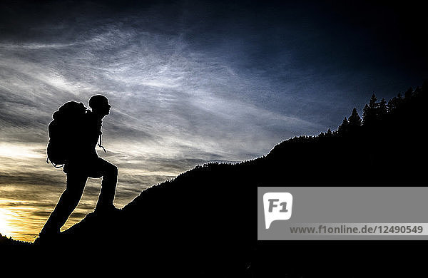 Ein Wanderer steht bei Sonnenuntergang auf einem kleinen Felsen in der Nähe von Wallgau  Deutschland. Im Hintergrund ist die Baumgrenze eines nahen Berges zu sehen.
