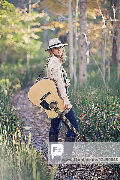 Eine junge Folksängerin posiert im Wald mit ihrer Gitarre.
