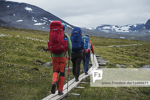 Hikers walk on wooden planks between Alesjaure and Tj?§ktja  Kungsleden trail  Lapland  Sweden