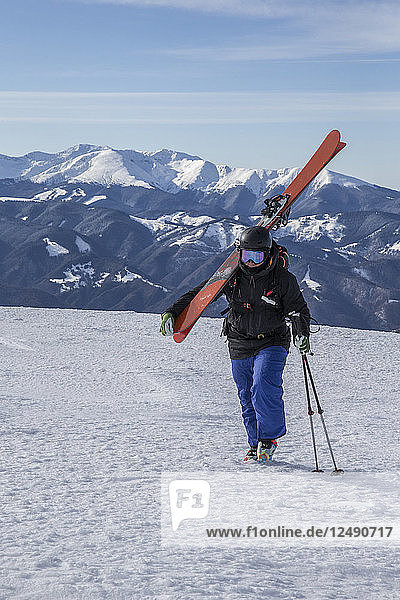 Skifahrer  der auf den Gipfel des Berges zugeht und seine Skier auf der Schulter trägt