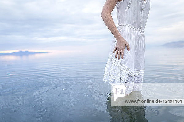 Eine junge Frau steht in einem See mit einem weiten Himmel.