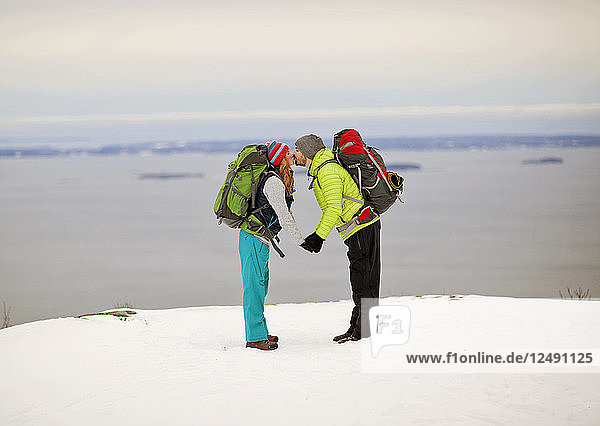 Ein Paar  das sich auf einem Berg im Winter entlang der Küste von Maine küsst