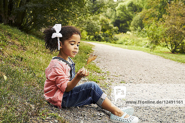 Ein kleines Mädchen sitzt auf der Seite der Straße und hält ein Herbstblatt