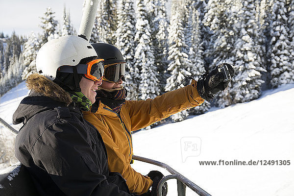 Teen skiers/snowboarders take picture on chairlift