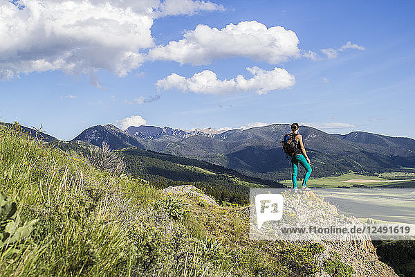 Woman takes a break from hiking to stand on a rock outcropping to look out into Montana's immense mountain landscape.