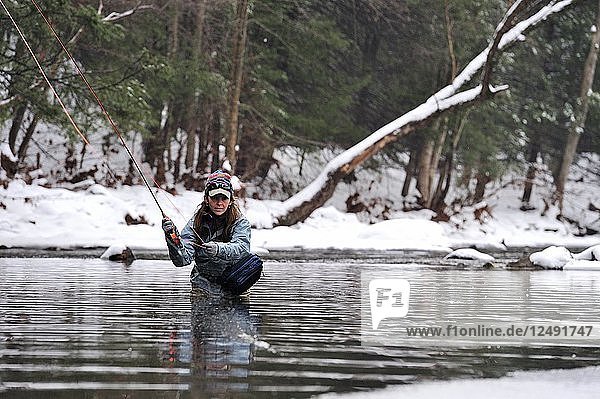 Eine junge Frau beim Fliegenfischen an einem verschneiten  kalten Wintertag. Sie angelt in einem kalten Winterbach.
