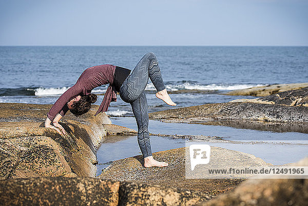 Frau macht Yoga an felsiger Küste