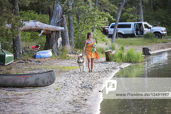 Eine junge Frau geht mit ihrem Hund an einem Teich spazieren  nachdem sie geschwommen ist