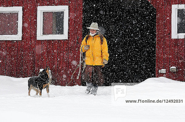 Frau schaut auf ihren Hund  während sie außerhalb der Scheune im Schnee spazieren geht