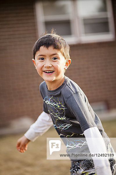 A 6 year old Japanese American boy runs smiling through the backyard.